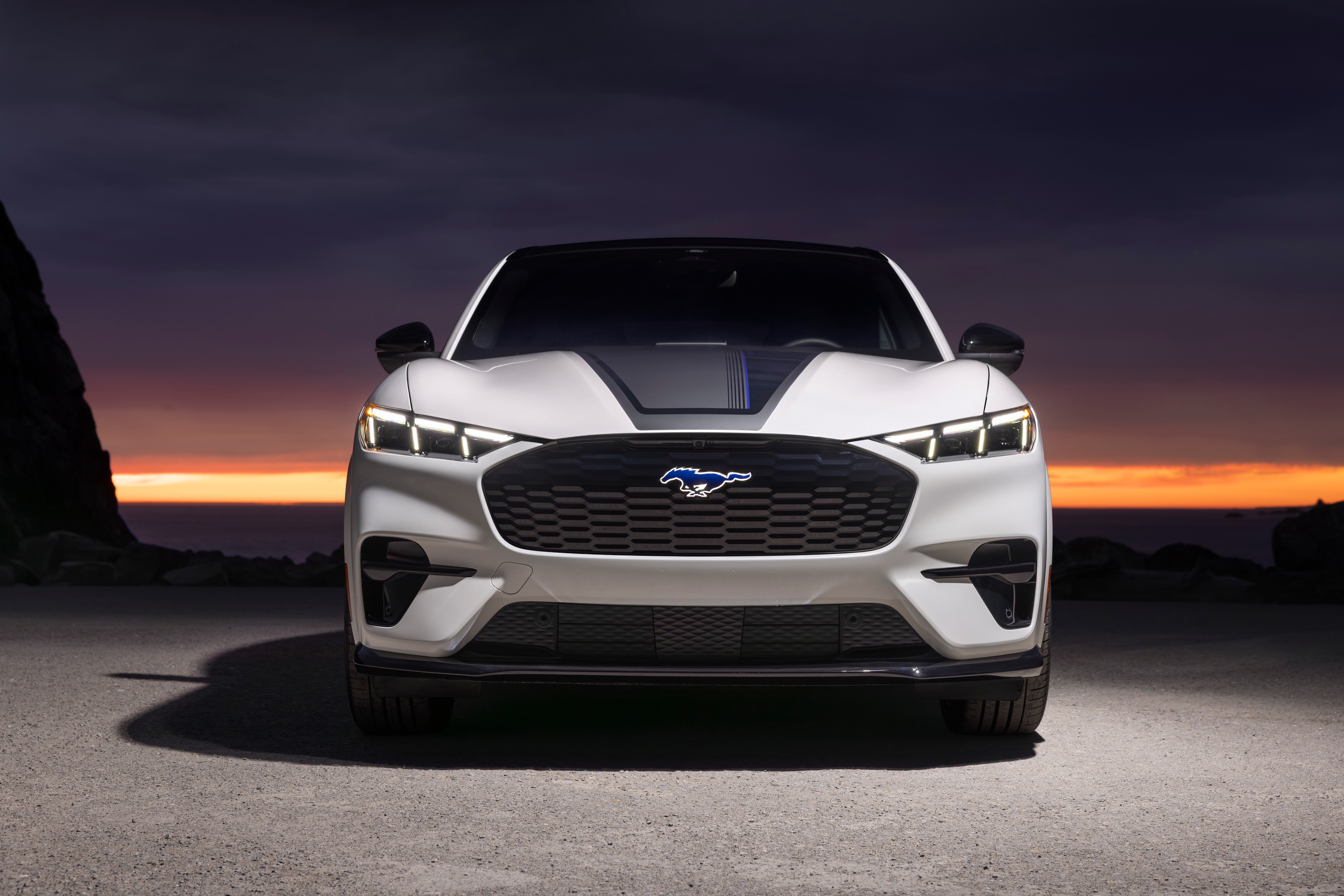 A whit Mustang Mach-E with the sunset behind.